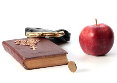 Metal bir para çantasının yanında olgun bir elma ve altın haçlı bir dini kitap.