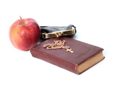 Metal bir para çantasının yanında olgun bir elma ve altın haçlı bir dini kitap.
