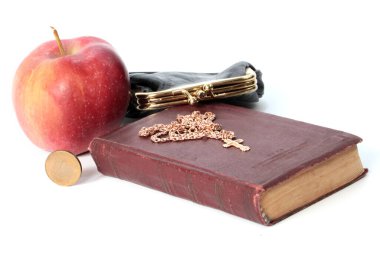 Metal bir para çantasının yanında olgun bir elma ve altın haçlı bir dini kitap.