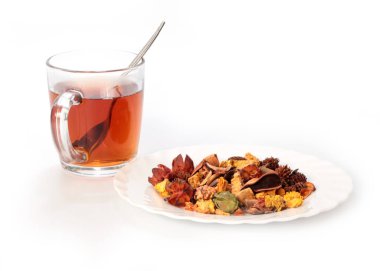 Bir bardak koyu siyah çay ve bir yığın kurutulmuş aromatik ot.