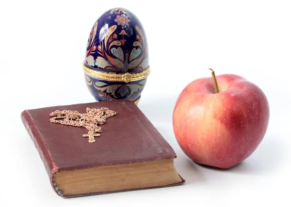 一个成熟的苹果 旁边有一本宗教书籍 上面有一个金色的十字架和一个复活节彩蛋 — 图库照片