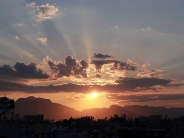 Akşamları güneş ışınları ve şehir binalarının çatısının üstündeki bulutlar.