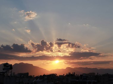 Akşamları güneş ışınları ve şehir binalarının çatısının üstündeki bulutlar.