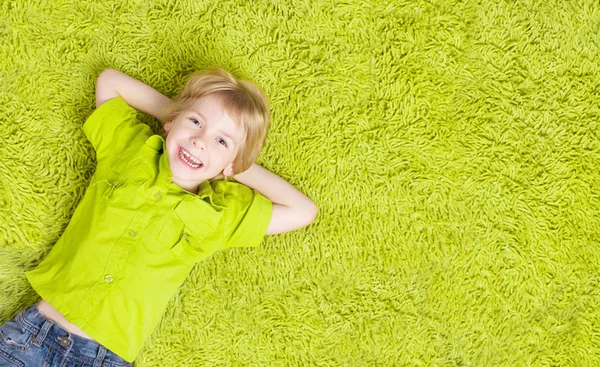 Niño acostado sobre una alfombra verde. Niño sonriente feliz —  Fotos de Stock