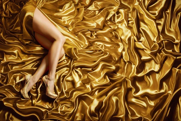 Vrouw been op gouden zijde stof achtergrond, Sexy Fashion Model benen in gouden schoenen — Stockfoto