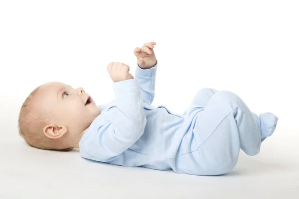 Μωρό ξαπλωμένη ανάσκελα, ευτυχισμένο παιδί βρέφος ντυμένος με μπλε φορμάκι, παιδί σε λευκό — Φωτογραφία Αρχείου