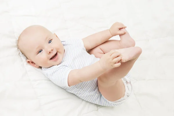 Bambino sdraiato sulla schiena, Ragazzo sorridente felice che tiene le gambe nelle mani, Neonato su bianco — Foto Stock