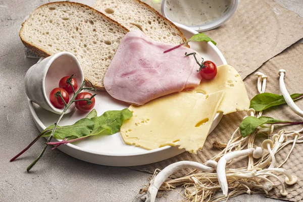 Salatalık, kiraz, peynir, jambon, domates, ekmek, yeşil ve mantarlar beyaz tabakta.
