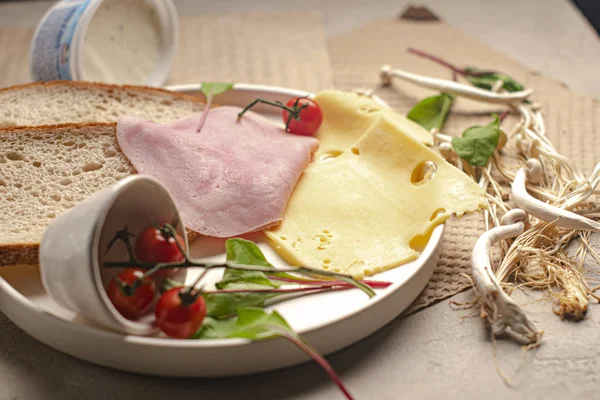 Salatalık, kiraz, peynir, jambon, domates, ekmek, yeşil ve mantarlar beyaz tabakta.