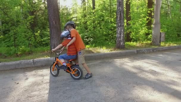 Старший ребенок учит своего младшего брата кататься на велосипеде — стоковое видео