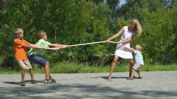 Three happy kids playing tug-of-war in city park with mum. — Stock Video