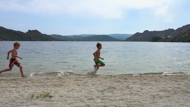 Два мальчика бегут по пляжу в замедленной съемке — стоковое видео
