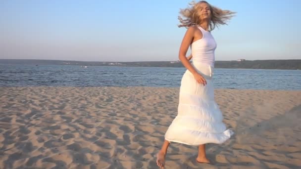 Счастливая молодая женщина в белом платье танцует на пляже — стоковое видео