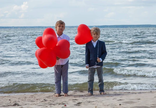 Niños de pie con globos rojos en la orilla del mar — Foto de Stock