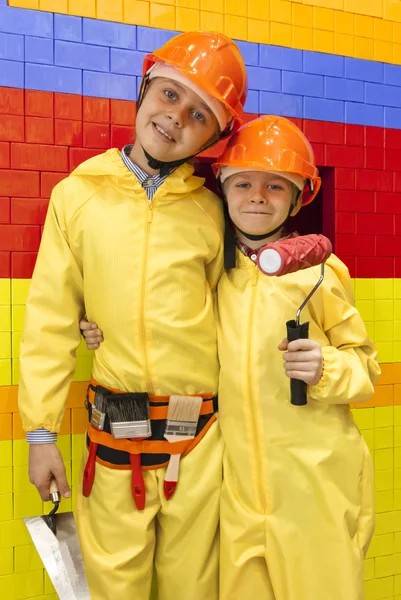 Boys wearing hard hats and yellow overalls are holding construction tools — Stock Photo, Image