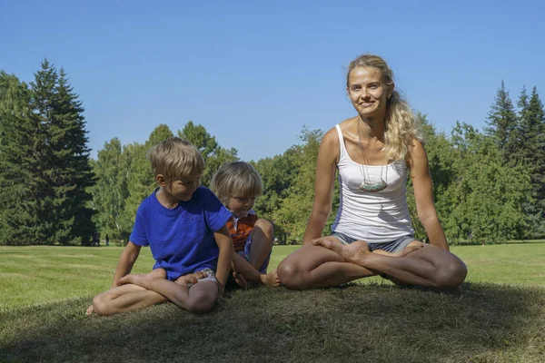 Yeşil çimenlerin üzerinde yoga yaparken mutlu anne — Stok fotoğraf