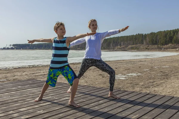 Jovem mulher e menino de pé em ioga posar na praia — Fotografia de Stock
