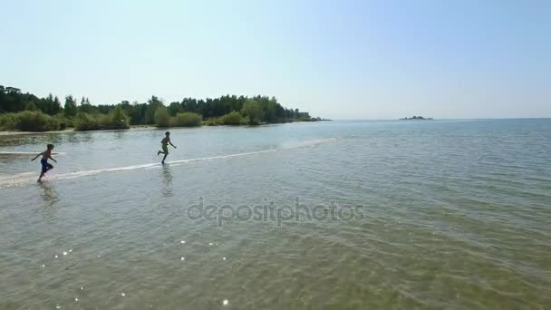 Three Kids run along a narrow strip of coast to the sea. — Stock Video