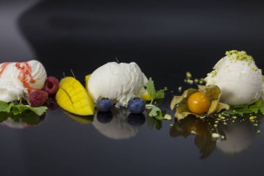 Çilek syrop, yaban mersini, fındık ve mango siyah yüzeyi ile vanilyalı dondurma kaşık toz.