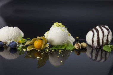 Vanilyalı dondurma kaşık toz çikolata syrop, meyveler, fındık ve mango siyah yüzeyi ile.