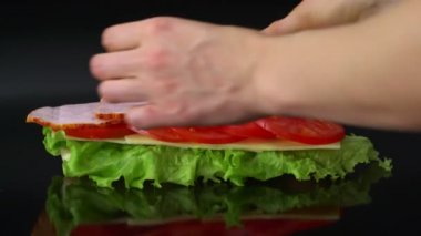 kadın siyah arka plan üzerine domates, peynir, jambon ve marul ile büyük sandviç yapma
