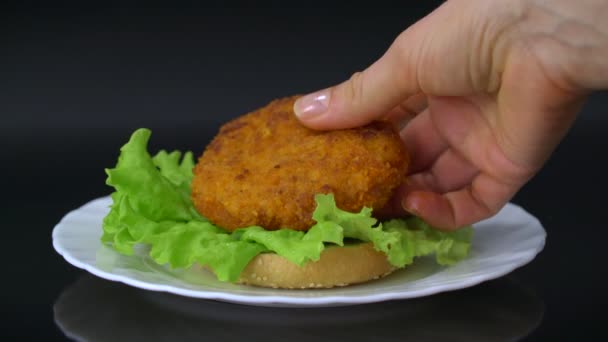 用鸡肉排 西红柿 生菜和欧芹在白色盘子上制作美味的汉堡 紧贴黑色背景 — 图库视频影像
