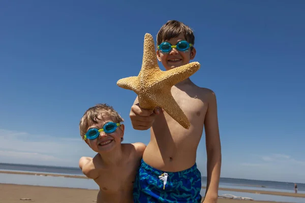 快乐地笑着 穿着护目镜 在热带海滩上抱着海星的游客男孩 — 图库照片