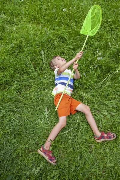 Menino Loiro Sorrindo Deitado Uma Grama Verde Com Uma Rede — Fotografia de Stock