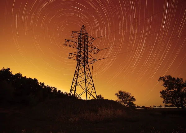 transmission tower against star trails in night sky