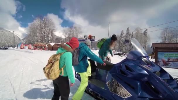 Vrienden hebben plezier op het skigebied. Jonge glimlachende mensen op een sneeuwscooter. Drie personen op een sneeuwscooter genieten van de winterdag. — Stockvideo