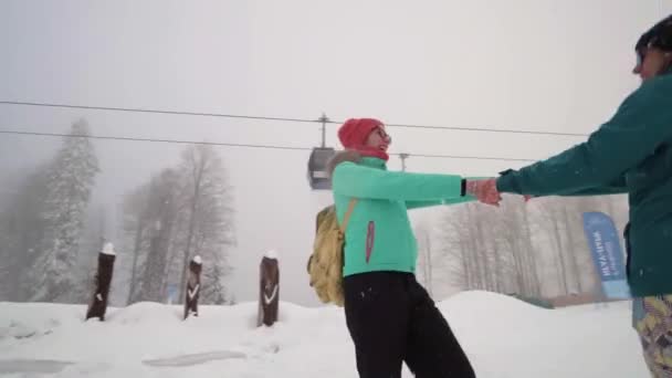 Vänner ha kul på skidorten. Sällskap av vänner som har kul på semester i vinterbergen. Två tjejer njuter av den snöiga dagen på skidorten. Flickor som håller händer och snurrar . — Stockvideo