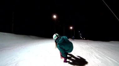 Dişi snowboardcu kayak pistinde kuyrukta yavaşça süzülüyor. Kuyruk presi yapan kız. Snowboardcu kuyruk kanadına basıyor. Genç kız serbest stil snowboard deneyimi yaşıyor. Gece kayak merkezinde at sürerken