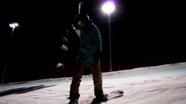 Langzame beweging van vrouwelijke snowboarder rijdt onder de nachtelijke hemel aan de voorkant van de lichten. — Stockvideo