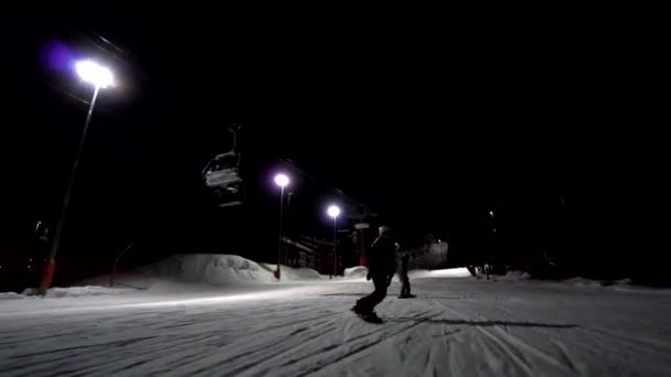 Snowboardåkare tagna från ansiktet är rida framåt till kameran Ski trail tänds på natten. Skidspår med belysning. Flickor ha kul på natten på skidorten. — Stockvideo