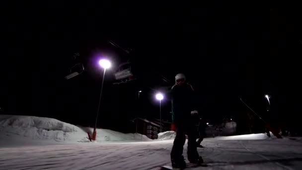 Långsam rörelse av snowboardåkare tagna från ansiktet är rida framåt till kameran Ski trail tänds på natten. Skidspår med belysning. Ridning på natten på skidorten. — Stockvideo