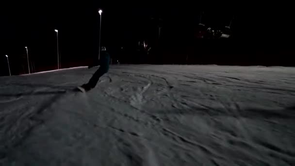 Ung kvinnlig snowboardåkare säker racing längs spåret ljus. Ridning på natten på skidorten. — Stockvideo