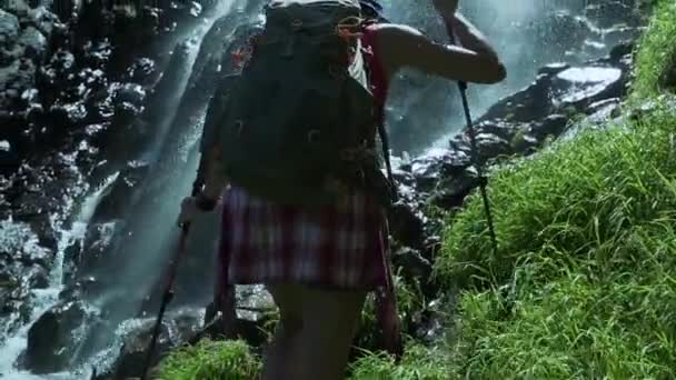 Hiker girl climb to the mountain waterfall. A hiker climbs to the marvel waterfall with trekking poles. Bottom view. — Stock Video