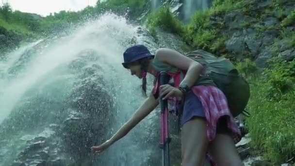 Un excursionista sube a la maravillosa cascada con bastones de trekking. Vista de abajo. Mujer joven disfruta de la cascada de montaña cristalina . — Vídeos de Stock