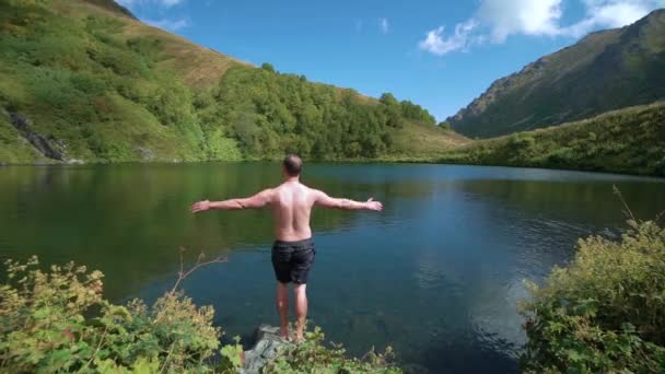 Vandrare stannar nära sjön, armarna utsträckta. Unge man vandrare når mountaim sjön och sträcker ut armen. Resultat i naturen — Stockvideo