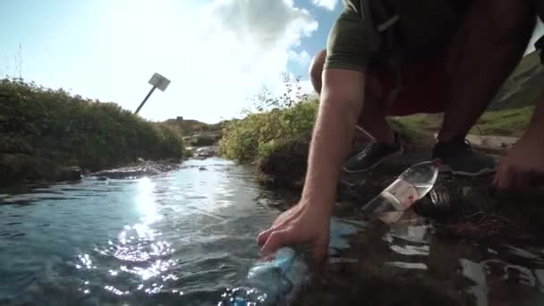 Туристы наполняют бутылку водой из горной реки . — стоковое видео