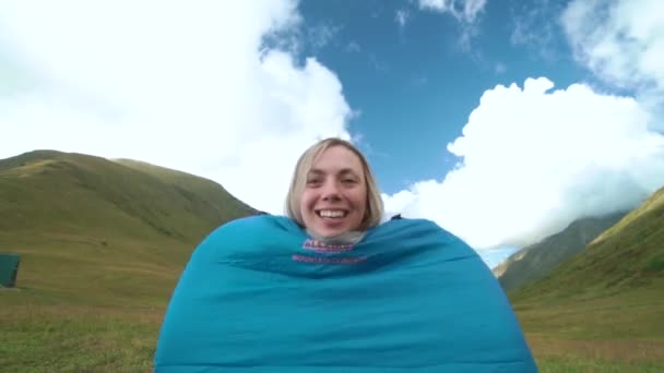 Young woman jumping in sleeping bag at sunset in the forest. Girl dances in sleeping bag on the magnifiscant green meadow between mountain. — Stock Video