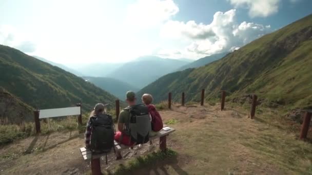 Jovens caminhantes relaxando no banco, vista panorâmica. Jovens caminhantes relaxando no banco de madeira do topo da montanha . — Vídeo de Stock