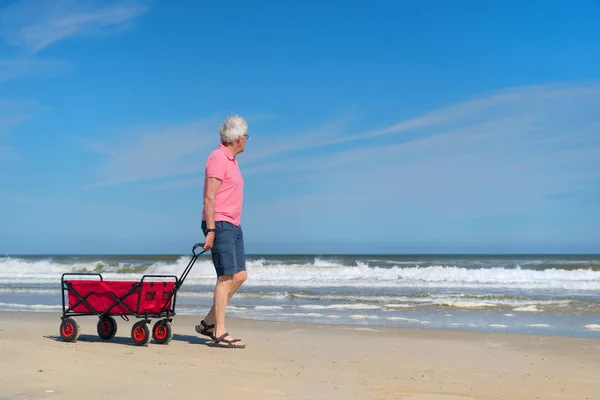 Senior geht mit Einkaufswagen am Strand spazieren — Stockfoto