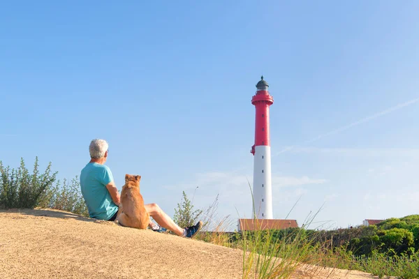 Man and dog sitting near lighthouse at the beach — Stock Photo, Image