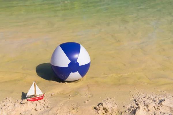 おもちゃのボートと水に浮かぶインフレータブルブルーとホワイトビーチボール — ストック写真