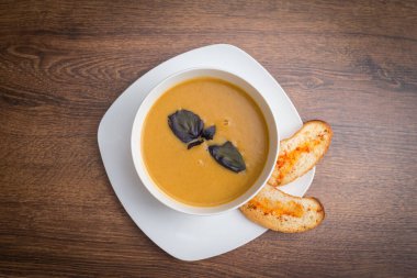 Baharatlı kırmızı mercimek çorbası, otlar, rustik metal tencere ve kaselerde ekmek, ahşap fon, üst manzara.