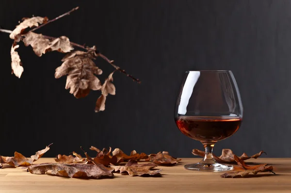 Snifter of brandy and dried oak leaves — Stock Photo, Image
