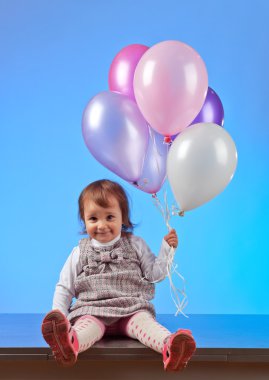  Mavi arka planda balonları olan küçük bir kız.