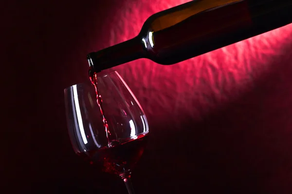 Láhve a sklenice červeného vína na tmavém pozadí — Stock fotografie