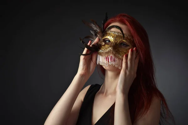 Schöne rothaarige Frau mit Karnevalsmaske auf schwarzem Hintergrund — Stockfoto